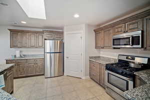 Kitchen featuring appliances with stainless steel finishes, light tile patterned floors, a skylight, and light stone counters