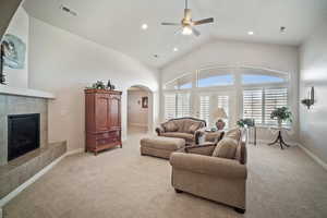 Living room with ceiling fan, light carpet, high vaulted ceiling, and a tiled fireplace