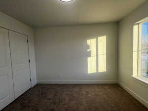 Unfurnished bedroom featuring a closet, multiple windows, and dark colored carpet