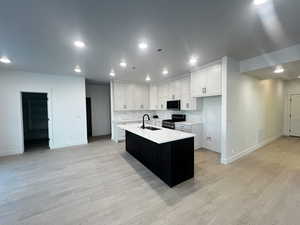 Kitchen with white cabinets, an island with sink, stainless steel stove, and tasteful backsplash