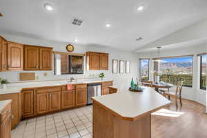 Kitchen featuring sink, stainless steel dishwasher, lofted ceiling, decorative light fixtures, and a kitchen island