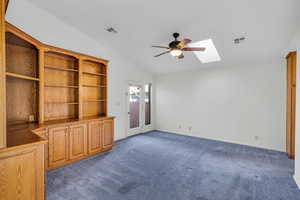 Unfurnished living room with dark colored carpet, ceiling fan, and vaulted ceiling with skylight