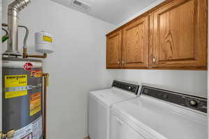 Washroom with washing machine and dryer, cabinets, and gas water heater