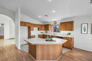 Kitchen with dishwasher, light wood-type flooring, a kitchen island, and lofted ceiling