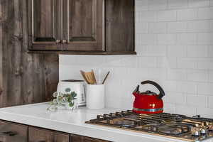 Kitchen featuring stainless steel gas cooktop, backsplash, and dark brown cabinets