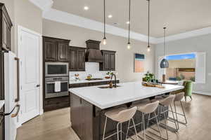 Kitchen featuring white appliances, hanging light fixtures, a center island with sink, a breakfast bar area, and sink