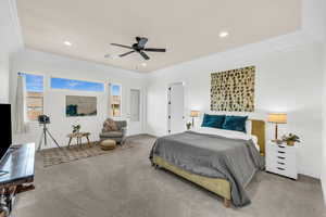 Bedroom with ceiling fan, light colored carpet, and a tray ceiling