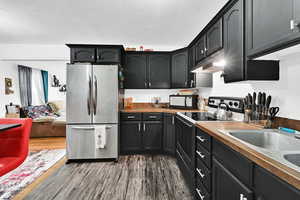 Kitchen with stainless steel refrigerator, sink, a textured ceiling, electric stove, and hardwood / wood-style flooring