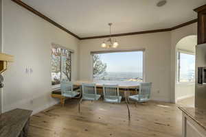 Dining area with a wealth of natural light, a chandelier, crown molding, and light hardwood / wood-style floors