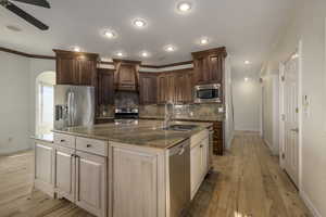 Kitchen with sink, stainless steel appliances, tasteful backsplash, light hardwood / wood-style floors, and a kitchen island with sink