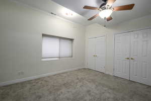 Unfurnished bedroom with ceiling fan, light colored carpet, crown molding, and multiple closets