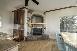 Living room with light hardwood / wood-style flooring, a stone fireplace, ceiling fan, and crown molding