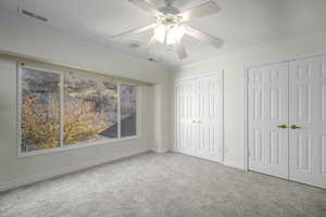 Unfurnished bedroom featuring ceiling fan, crown molding, light carpet, and two closets