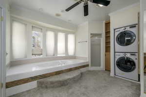 Laundry room with ceiling fan, stacked washing maching and dryer, light carpet, and ornamental molding