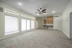 Unfurnished living room with light carpet, ceiling fan, and crown molding