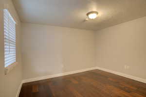 Empty room with a textured ceiling and dark wood-type flooring