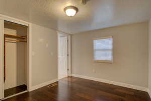 Unfurnished bedroom with dark hardwood / wood-style flooring, a textured ceiling, and a closet