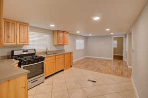 Kitchen featuring light tile patterned flooring, sink, light brown cabinetry, and stainless steel gas range