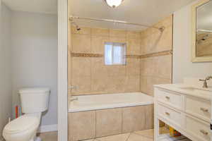 Full bathroom with tiled shower / bath combo, tile patterned floors, a textured ceiling, toilet, and vanity