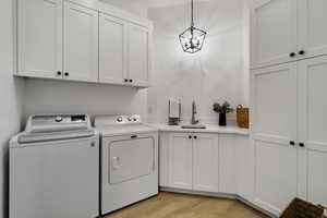 Laundry area with washer and clothes dryer, cabinets, an inviting chandelier, sink, and light hardwood / wood-style floors