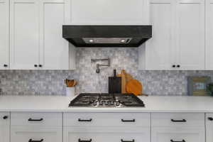 Kitchen featuring exhaust hood, white cabinetry, backsplash, and stainless steel gas cooktop