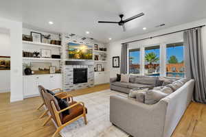 Living room with ceiling fan, light hardwood / wood-style floors, and a fireplace