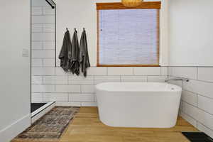 Bathroom featuring shower with separate bathtub, wood-type flooring, and tile walls