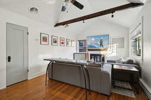 Living room featuring hardwood / wood-style flooring, lofted ceiling with beams, a baseboard radiator, and a brick fireplace