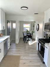 Kitchen featuring white cabinets, stainless steel appliances, light hardwood / wood-style flooring, and plenty of natural light