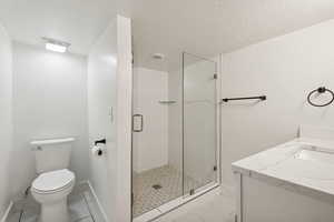 Bathroom featuring tile patterned floors, a textured ceiling, an enclosed shower, toilet, and vanity