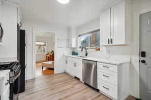 Kitchen with light stone countertops, white cabinetry, sink, appliances with stainless steel finishes, and light wood-type flooring