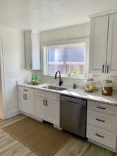 Kitchen featuring dishwasher, white cabinets, light wood-type flooring, and sink