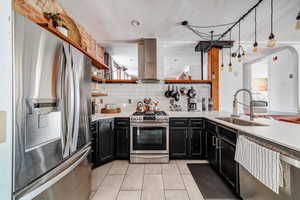 Kitchen with sink, wall chimney range hood, backsplash, light tile patterned flooring, and appliances with stainless steel finishes