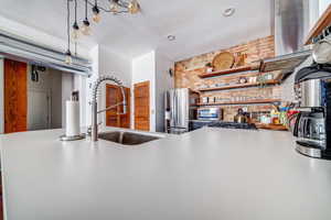 Kitchen with appliances with stainless steel finishes, sink, pendant lighting, and brick wall