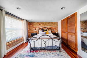 Bedroom with wood-type flooring, a closet, and brick wall