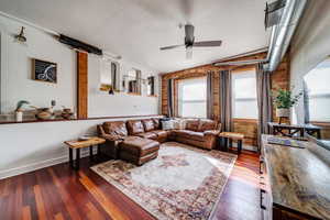 Living room featuring lofted ceiling, ceiling fan, dark wood-type flooring, and brick wall