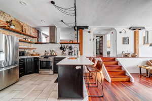 Kitchen featuring wall chimney range hood, sink, appliances with stainless steel finishes, kitchen peninsula, and a breakfast bar area