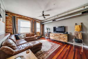 Living room with ceiling fan, brick wall, and dark hardwood / wood-style floors