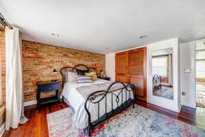 Bedroom featuring dark wood-type flooring and brick wall