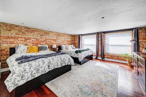 Bedroom featuring dark hardwood / wood-style floors and brick wall