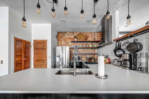 Kitchen featuring sink, wall chimney range hood, tasteful backsplash, stainless steel fridge with ice dispenser, and pendant lighting