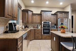 Kitchen with appliances with stainless steel finishes, tasteful backsplash, dark brown cabinets, and sink