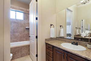 Bathroom featuring vanity, an inviting chandelier, tile patterned flooring, toilet, and tiled tub