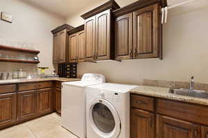 Clothes washing area featuring cabinets, separate washer and dryer, light tile patterned floors, and wet bar