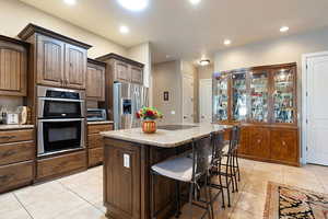 Kitchen featuring a center island, light stone countertops, light tile patterned floors, appliances with stainless steel finishes, and a kitchen bar