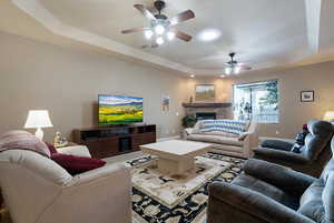 Living room featuring ceiling fan, a raised ceiling, and a fireplace