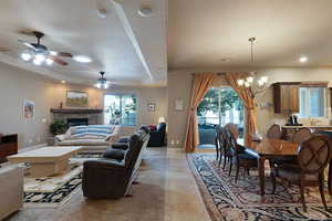 Tiled living room with ceiling fan with notable chandelier, a tray ceiling, a stone fireplace, and sink