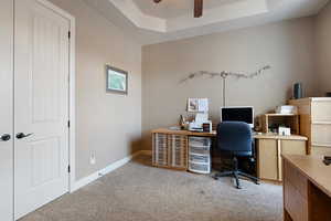 Carpeted home office featuring ceiling fan and a tray ceiling