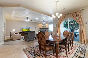 Dining area featuring ceiling fan with notable chandelier, light tile patterned flooring, and a tray ceiling