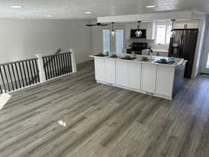 Kitchen featuring electric range, tasteful backsplash, stainless steel refrigerator with ice dispenser, a kitchen island with sink, and white cabinets